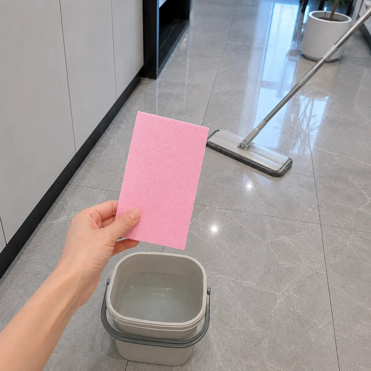 Customer holding a pink floor cleaning sheet near a mop and bucket